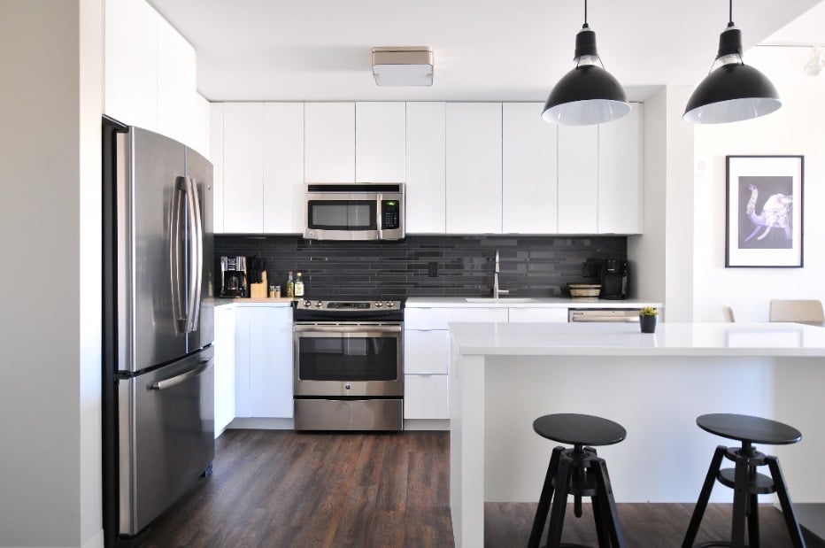 Modern kitchen with white countertops, black subway tiles, and stainless steel appliances.