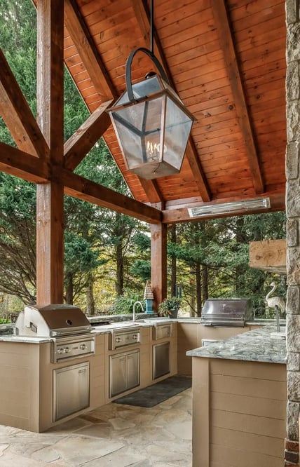 Elegant covered outdoor kitchen with stainless steel appliances and wooden beams.
