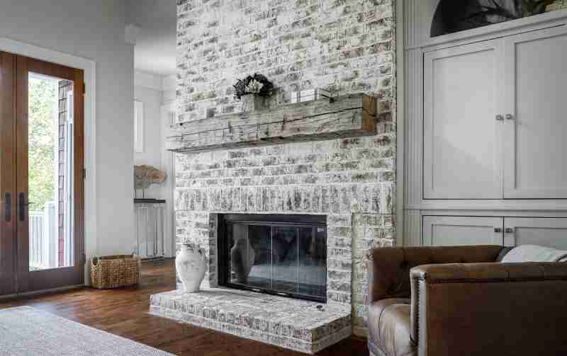 Living room featuring a white brick fireplace, rustic mantel, and leather sofa
