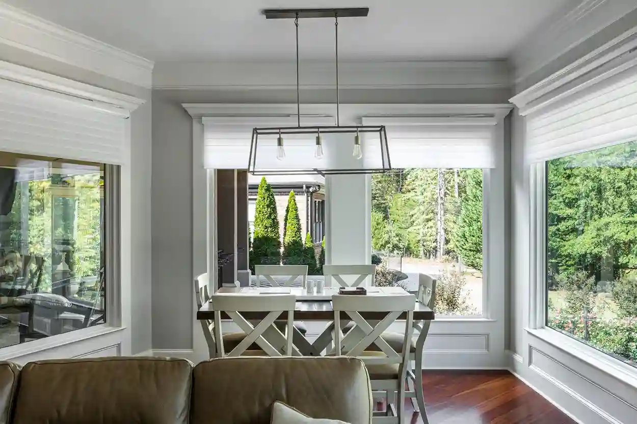  Airy dining space with natural light, modern rectangular chandelier, and a view of evergreen trees.