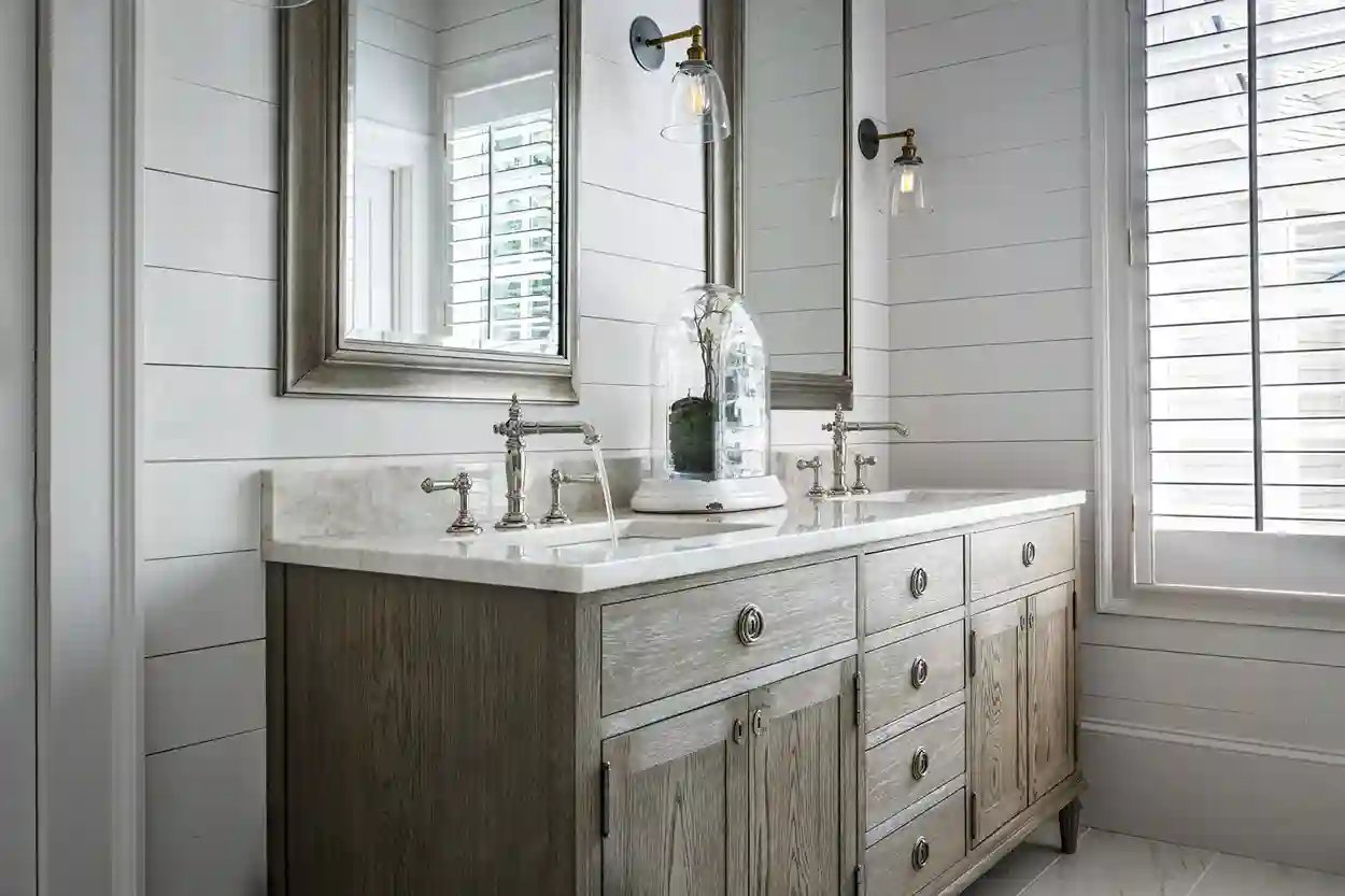 Traditional bathroom vanity with marble countertop and classic faucet, flanked by wall sconces and mirror