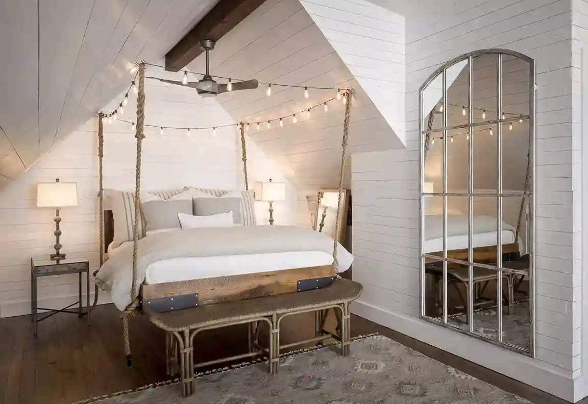 Cozy attic bedroom with hanging rope bed, shiplap walls, and large arched mirror