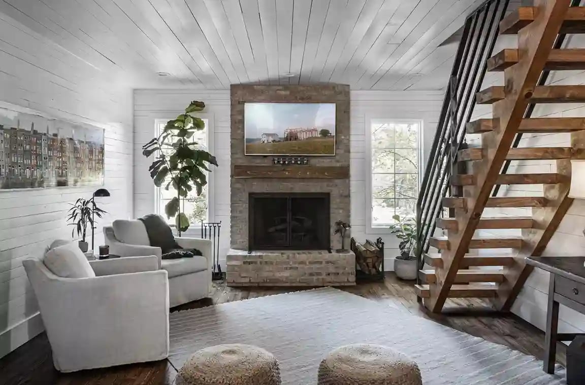 Bright living space with shiplap walls, stone fireplace, and modern staircase