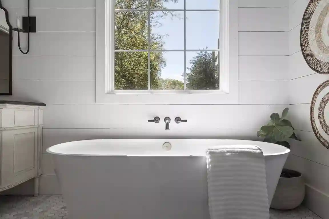 Freestanding white bathtub in a bright bathroom with shiplap walls and a large window