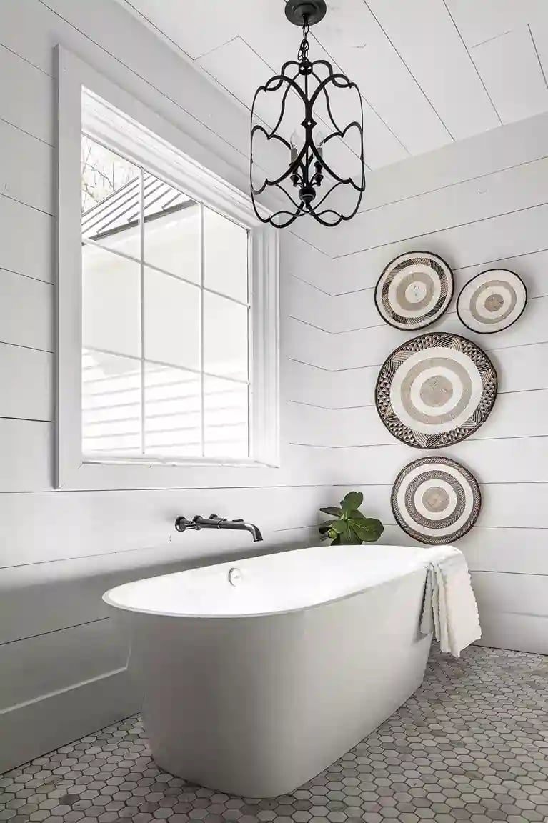 Chic farmhouse bathroom with freestanding tub, decorative wall plates, and a classic chandelier