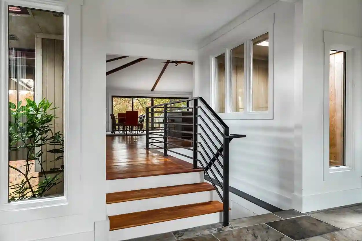 Elegant entryway with wooden stairs, black railing, and view into dining area.