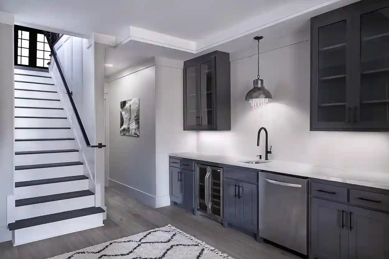 Modern kitchenette with dark cabinets and stylish pendant lighting near staircase.