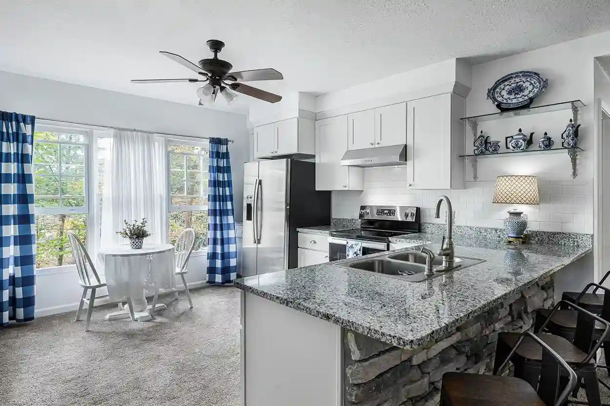  Charming kitchen with blue gingham curtains, granite countertops, and classic white cabinetry.