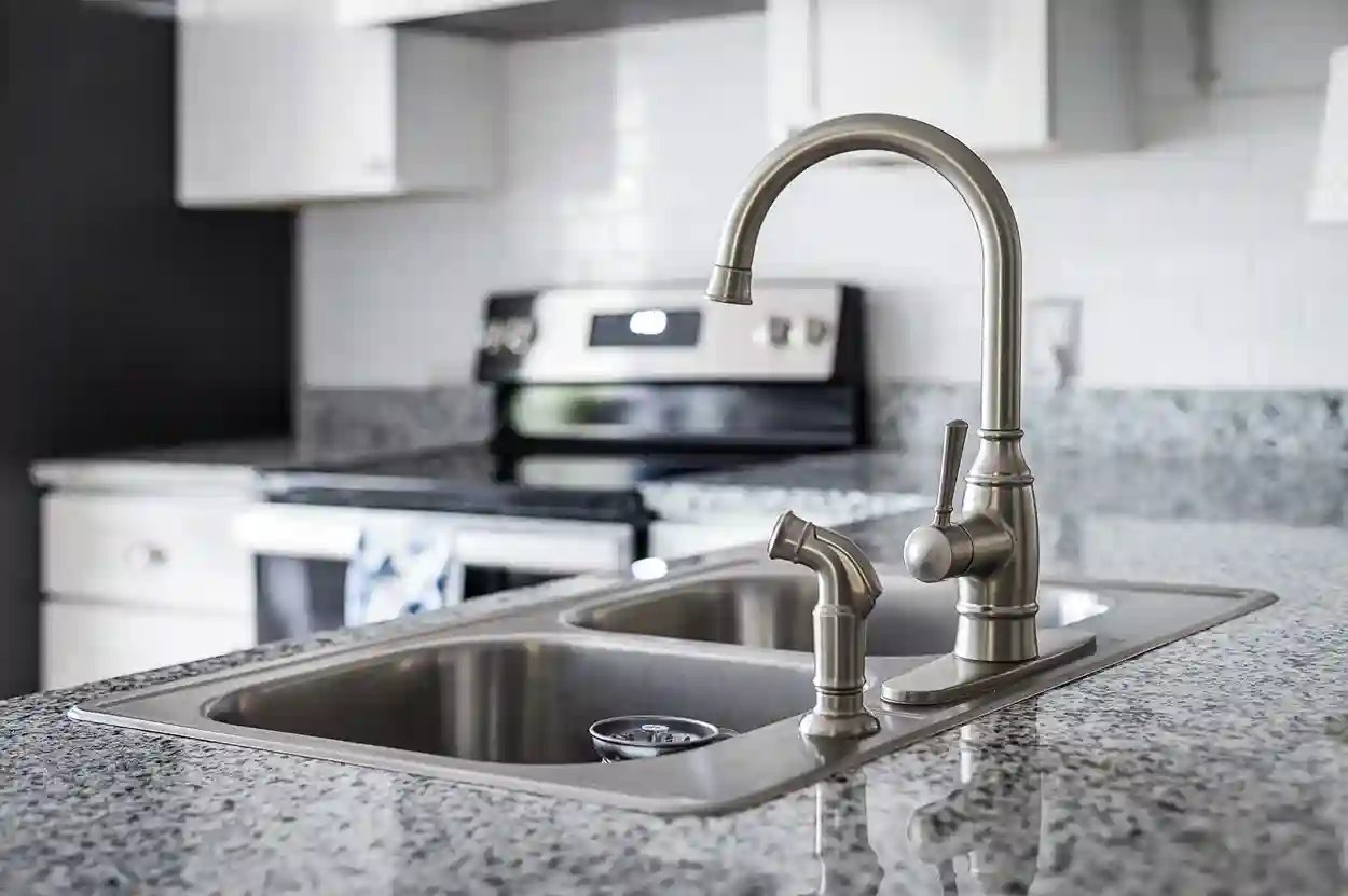 Modern kitchen sink with granite countertop and stainless steel faucet.
