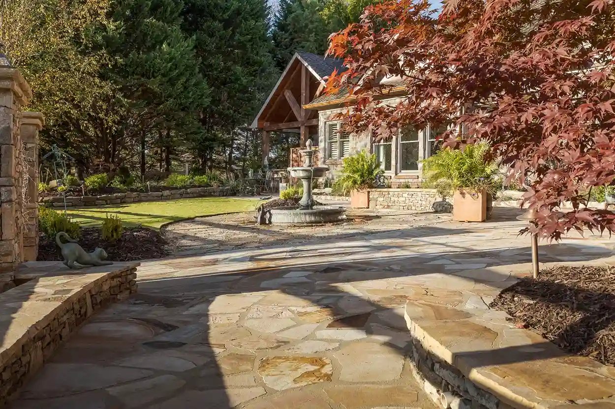 Stone-paved garden path leading to a rustic house with autumn foliage.