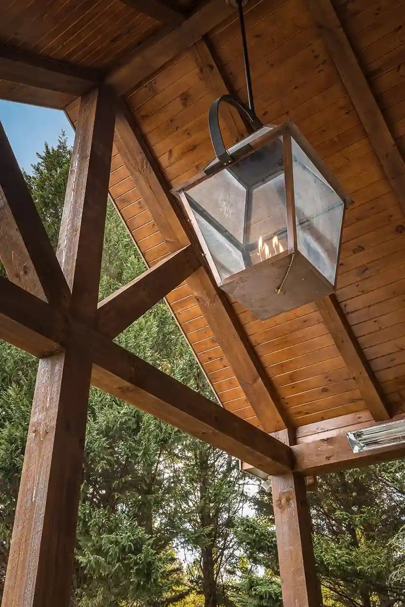 Outdoor wooden beam structure with a classic lantern against a backdrop of conifer trees.