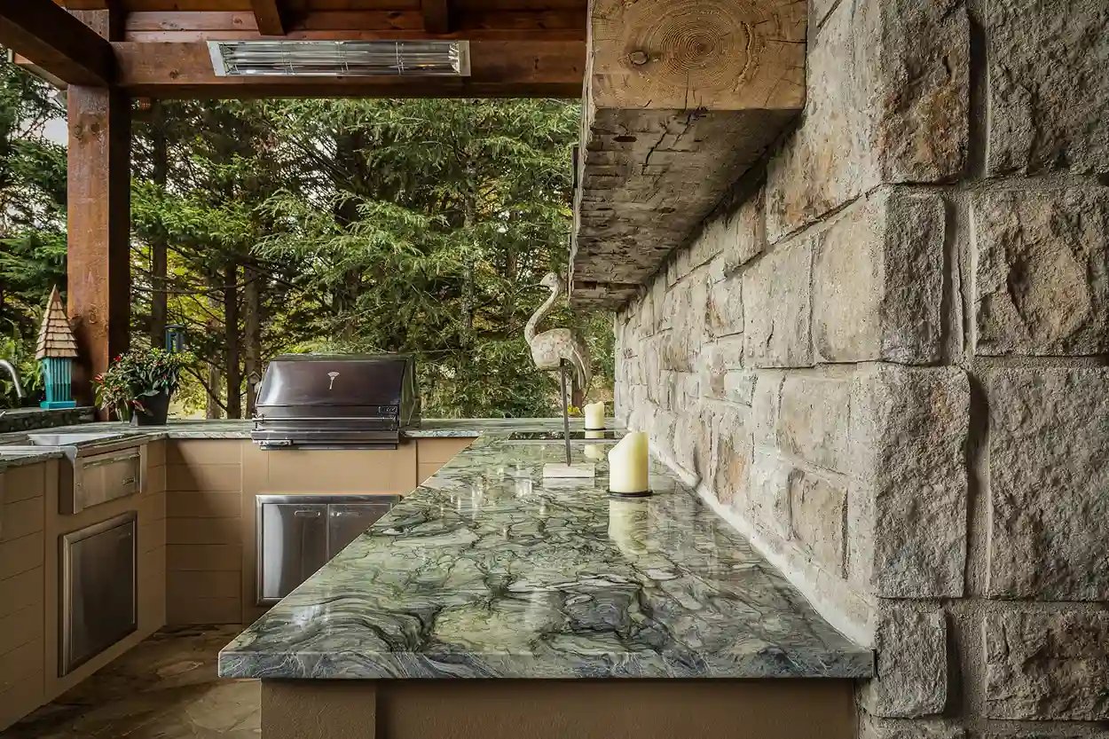 Outdoor kitchen with granite countertop and stone wall by Michael James Remodeling.