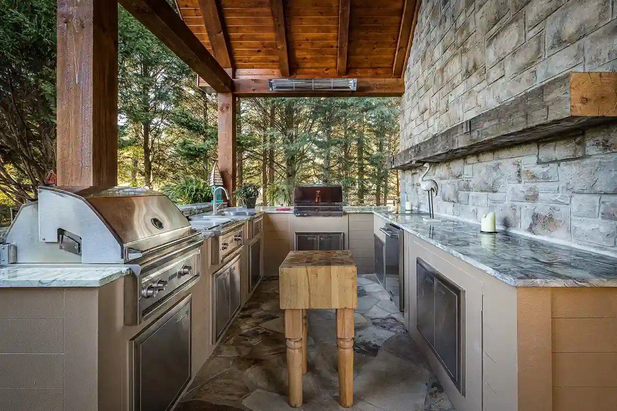Outdoor kitchen with stainless steel appliances and stone finishes under a wooden patio.