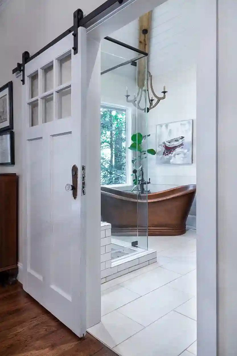 Sliding barn door opening to a modern bathroom with a freestanding copper tub and glass shower.
