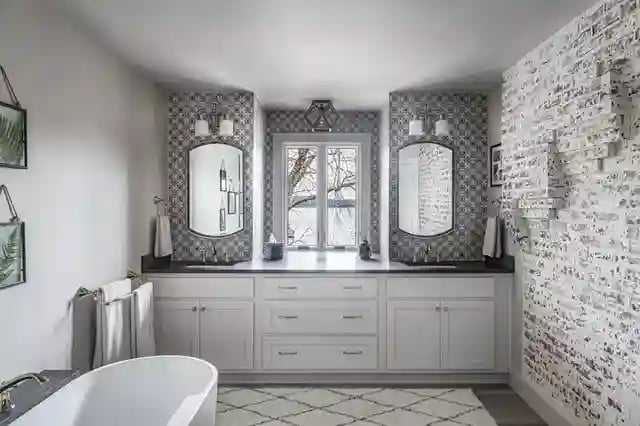 Chic bathroom with patterned wallpaper, dual sinks, ornate mirrors, and a freestanding bathtub.