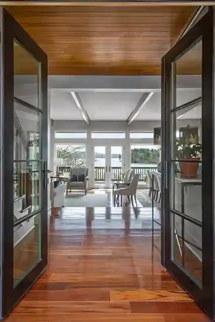 Glass doors opening to a wooden deck from a room with hardwood floors and ceiling.