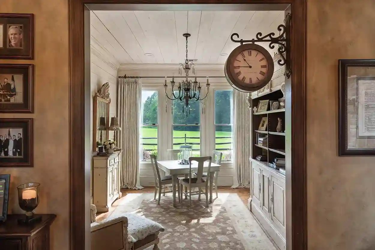 View into a classic dining space with a large wall clock, bookshelf, and natural lighting.