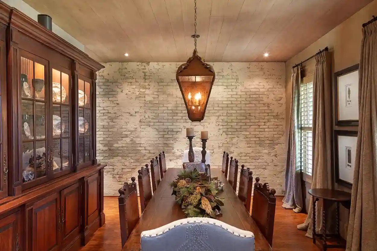 Elegant dining room with long wooden table, white-painted brick wall, and classic hanging lantern.