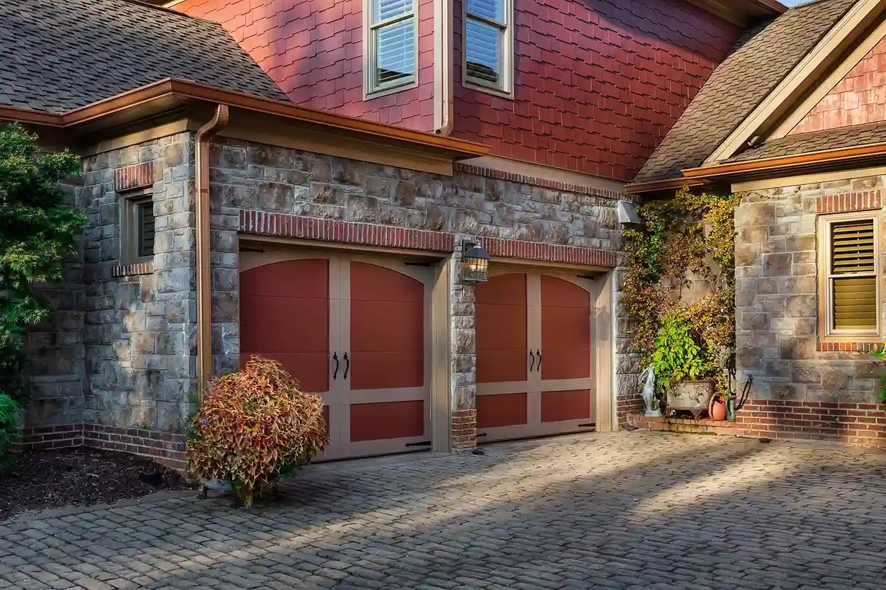 Traditional home exterior with red garage doors, stone facade, and cobblestone driveway.