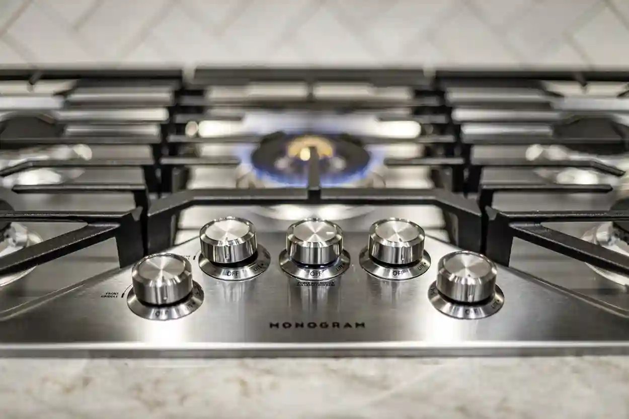 Stainless steel gas stove top with lit burner and control knobs from Monogram.