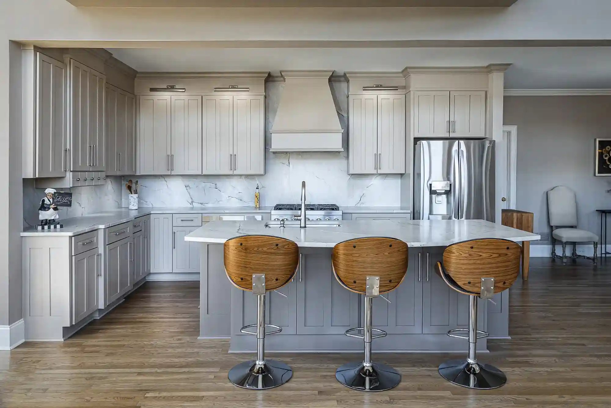 Sleek kitchen with taupe cabinets, marble backsplash, and contemporary wooden bar stools.