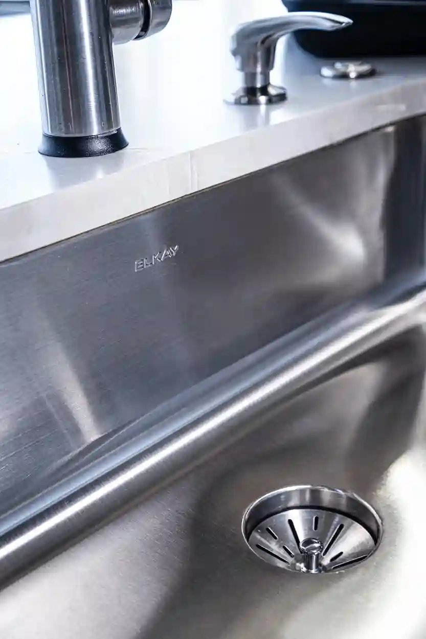 Close-up of a stainless steel Elkay kitchen sink with a modern faucet and marble countertop detail.