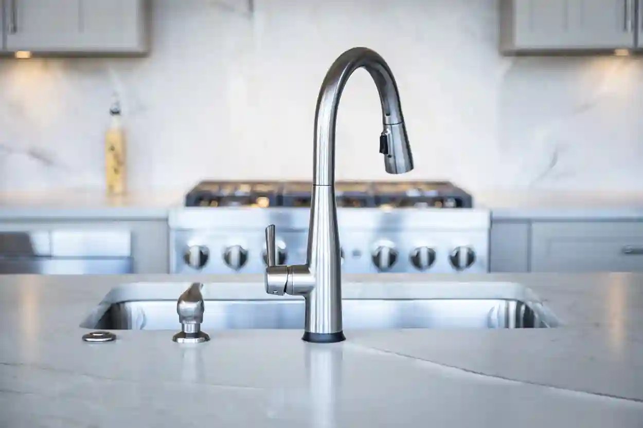 Modern stainless steel kitchen faucet over sink with blurred stove in background.
