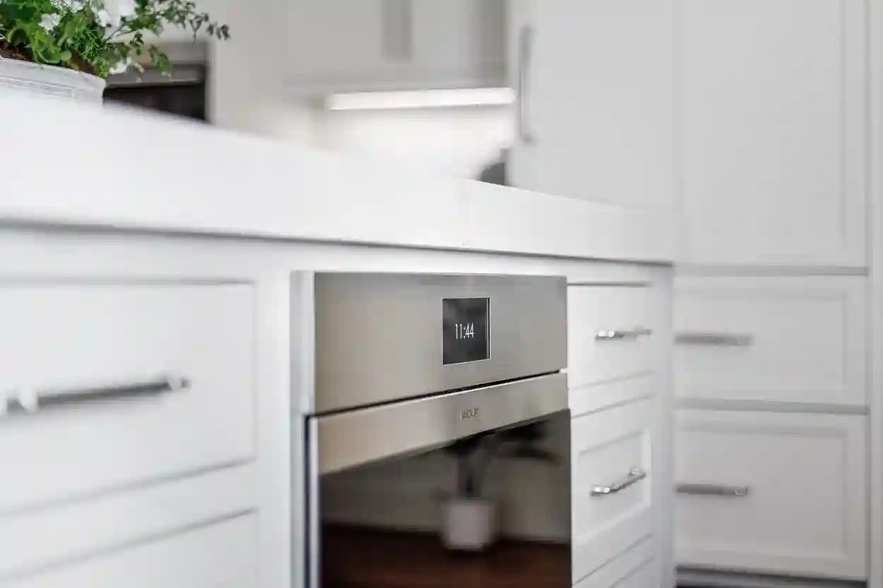  Modern kitchen detail showing a built-in stainless steel microwave drawer with digital clock display among white cabinets.