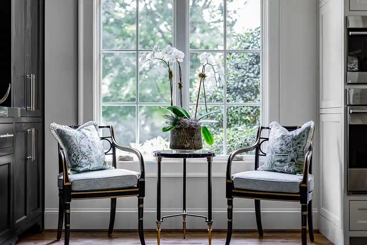 Chic sitting area with ornate chairs and a table featuring orchids by a sunlit window.