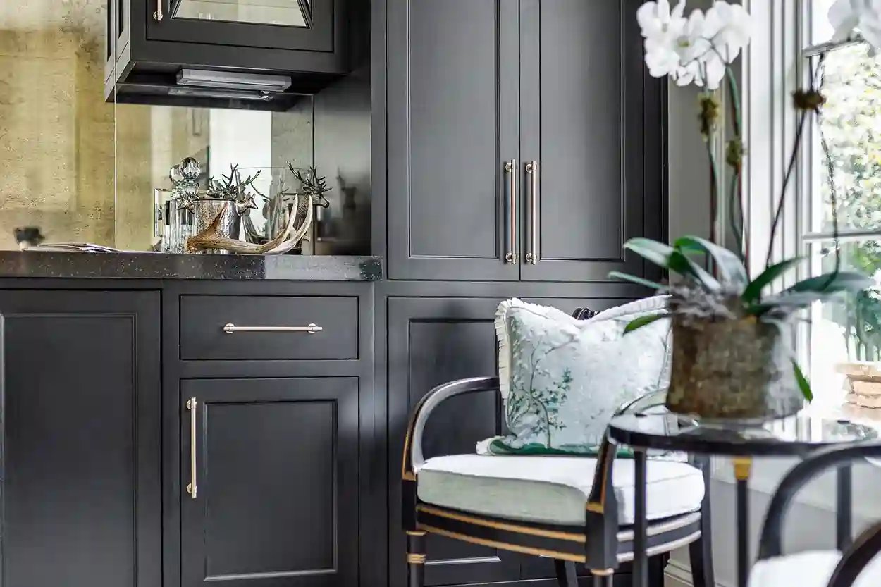 Elegant black cabinetry with brass hardware in a kitchen, complemented by decorative plants and a floral cushion.