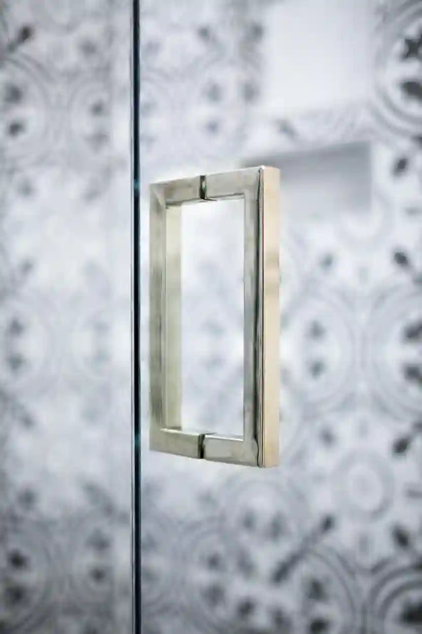 Close-up of a sleek shower door handle with patterned tile backdrop.