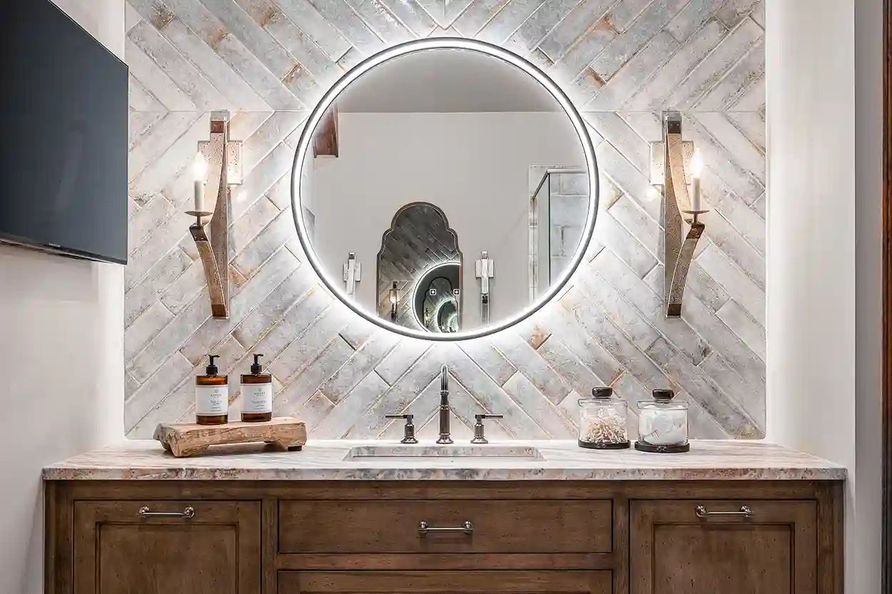 Elegant bathroom vanity with round illuminated mirror and herringbone tile backsplash