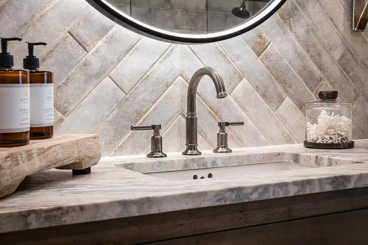 Luxurious bathroom vanity with marble countertop, herringbone tile backsplash, and round mirror