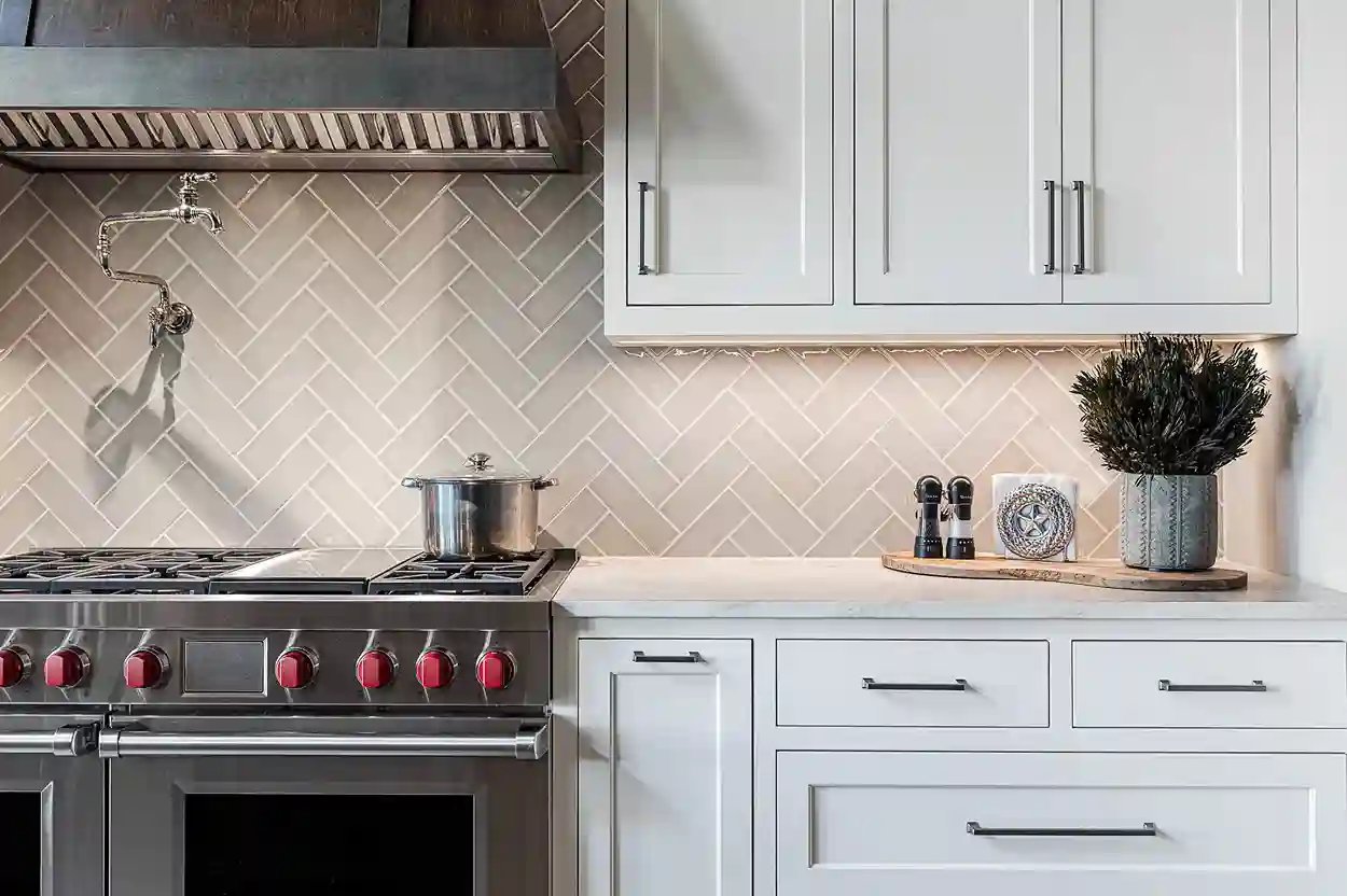 Elegant gas stove top with red knobs, stainless pot, and decorative kitchen items against a herringbone tile backsplash