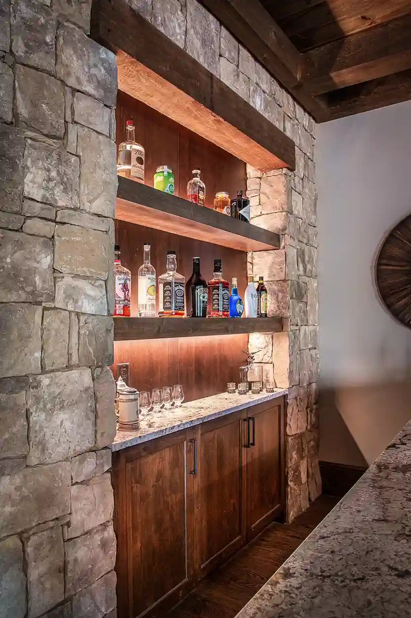 Stone accent wall with wooden shelving and a selection of spirits in a home bar by Michael James Remodeling.