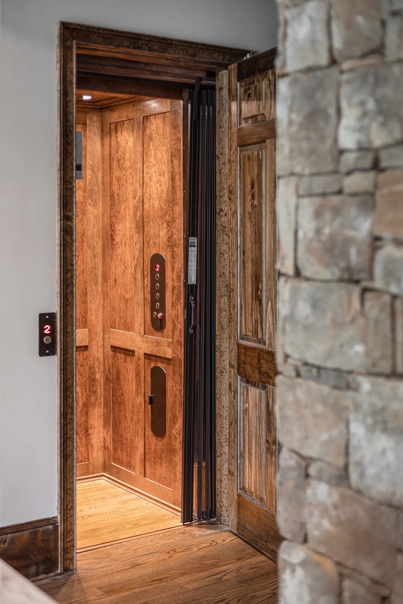 Elegant home elevator entrance with rich wooden doors and stone wall detailing.