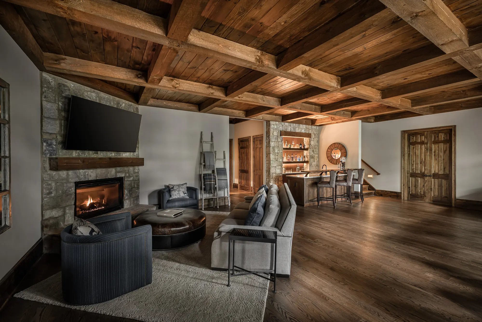  Spacious rustic living room with exposed beams, stone fireplace, and a home bar setup