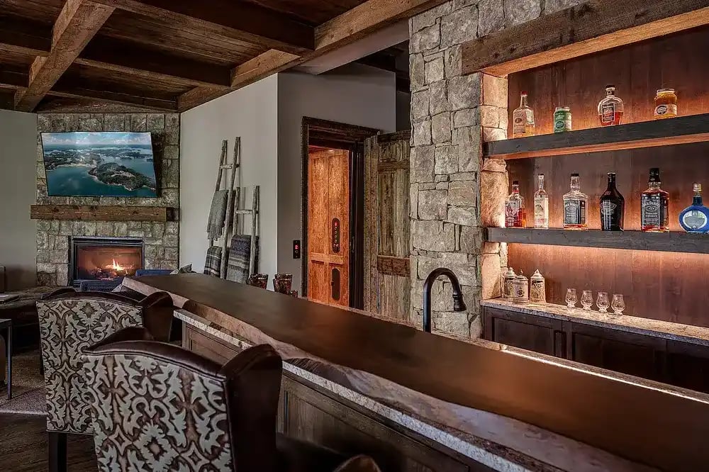  Cozy home bar area with stone fireplace and rustic wood shelving displaying spirits.