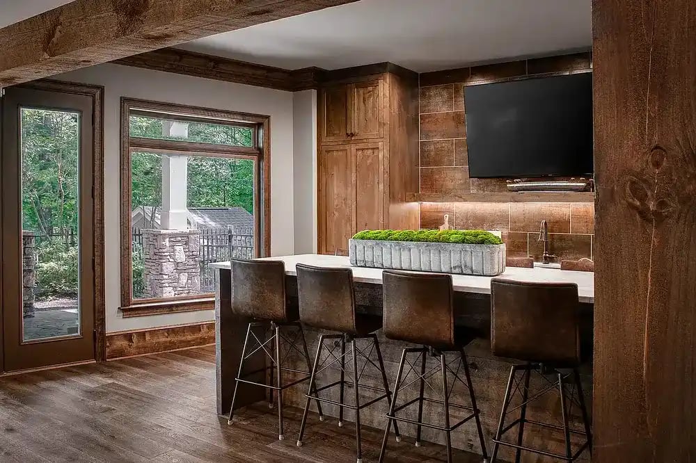 Custom indoor bar with wooden cabinets and leather stools in a modern home by Michael James Remodeling.
