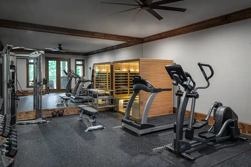Home gym with modern fitness equipment and infrared sauna designed by Michael James Remodeling.