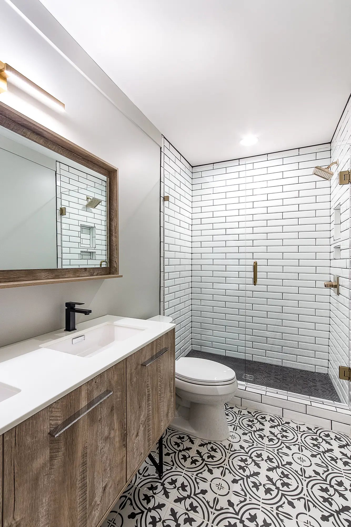 Modern bathroom with patterned floor tiles, subway-tiled shower, and wooden vanity