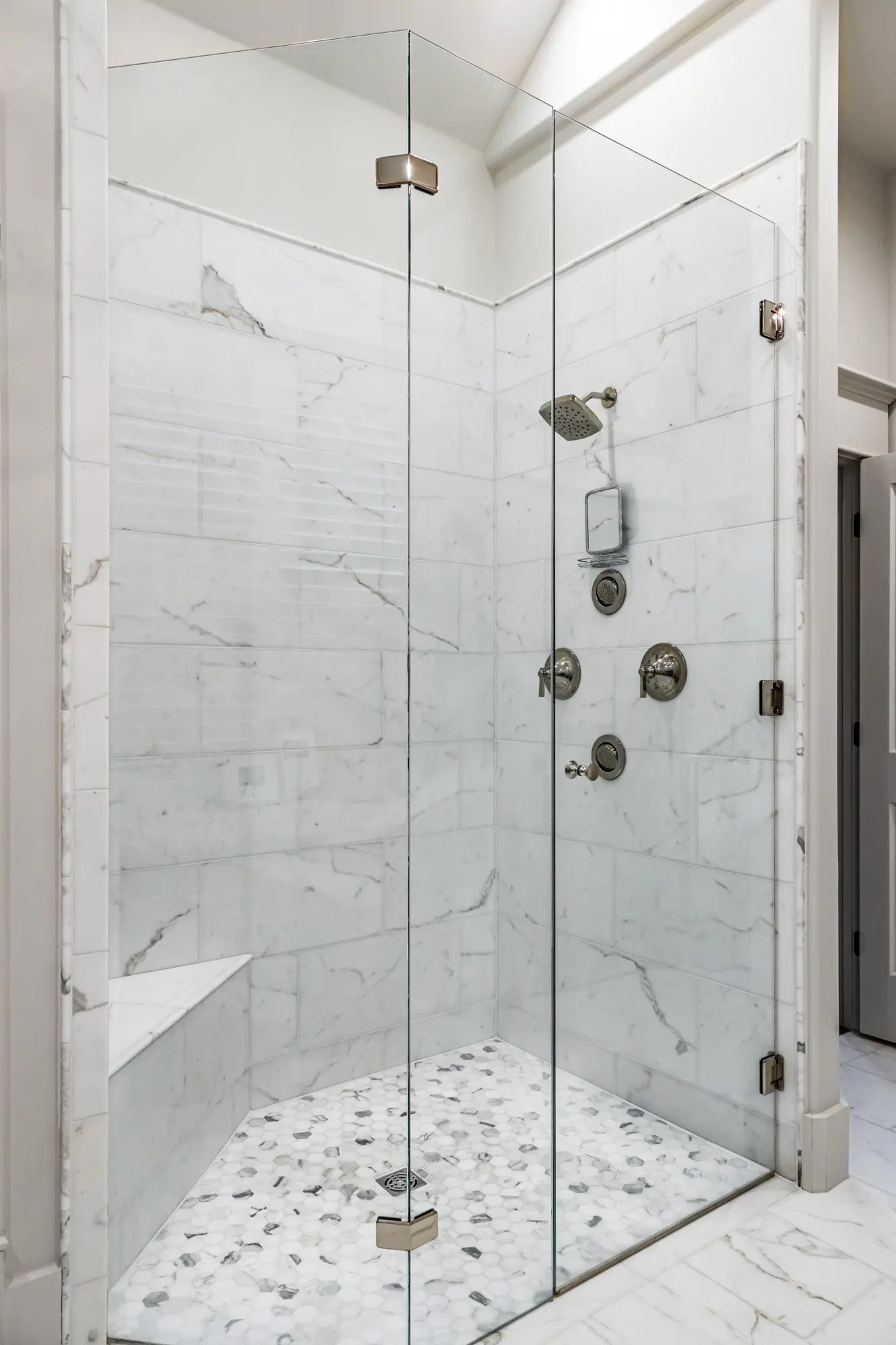 Elegant marble-tiled walk-in shower with pebble floor and modern chrome shower fixtures.