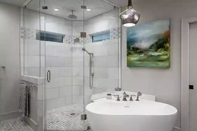 Elegant white bathroom with freestanding tub, glass shower, and artistic pendant light.