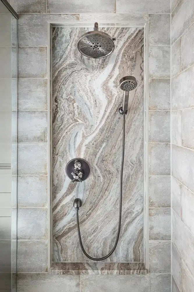  Elegant shower featuring a unique marble wall, dual showerheads, and brushed metal fixtures.