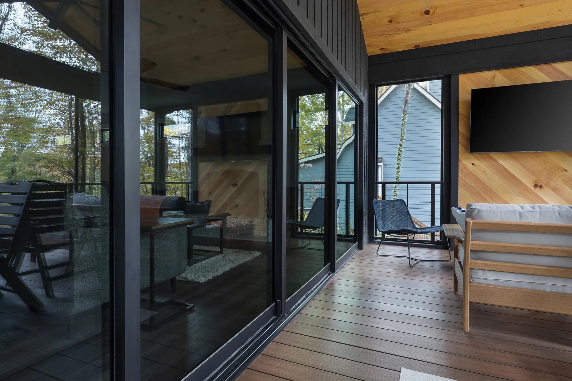 Modern screened porch with black trim, wooden elements, and comfortable outdoor furniture amidst nature.