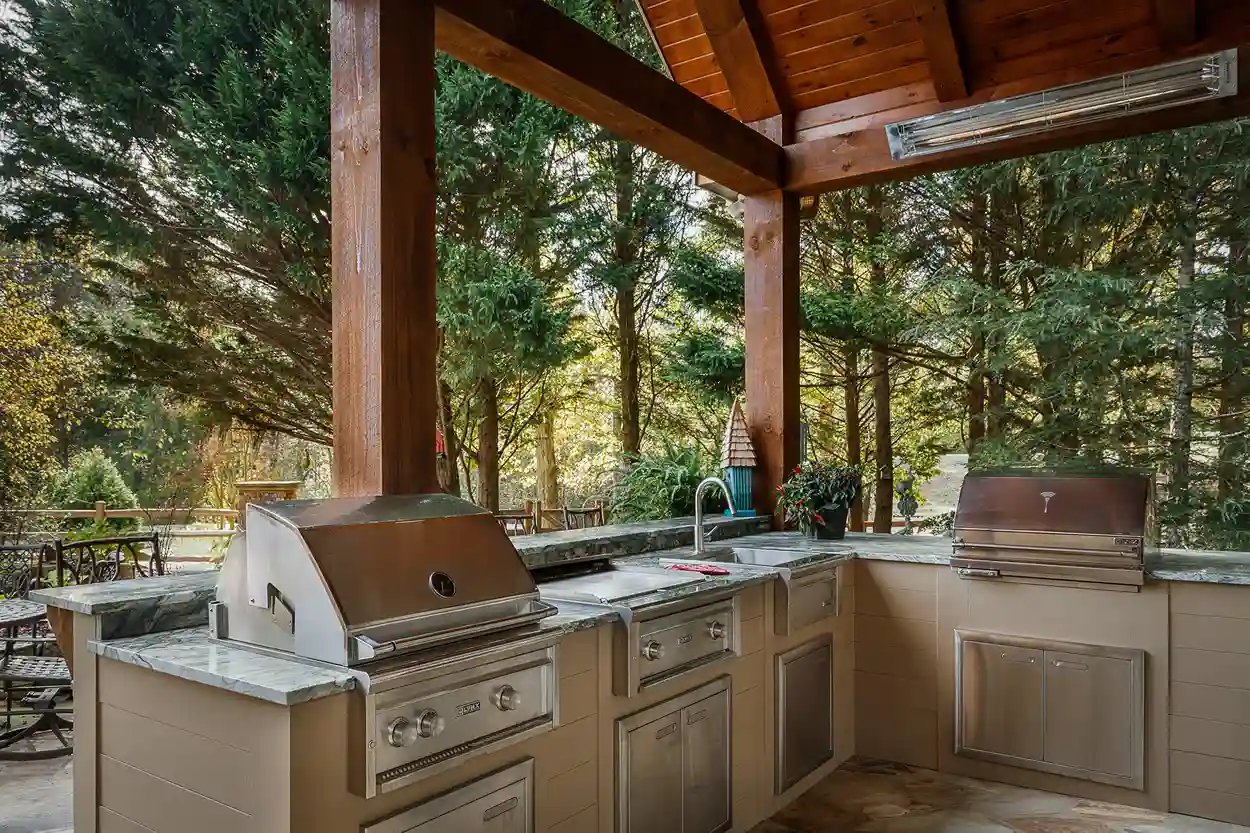 Outdoor kitchen with stainless steel grill and marble countertop under a wooden pergola