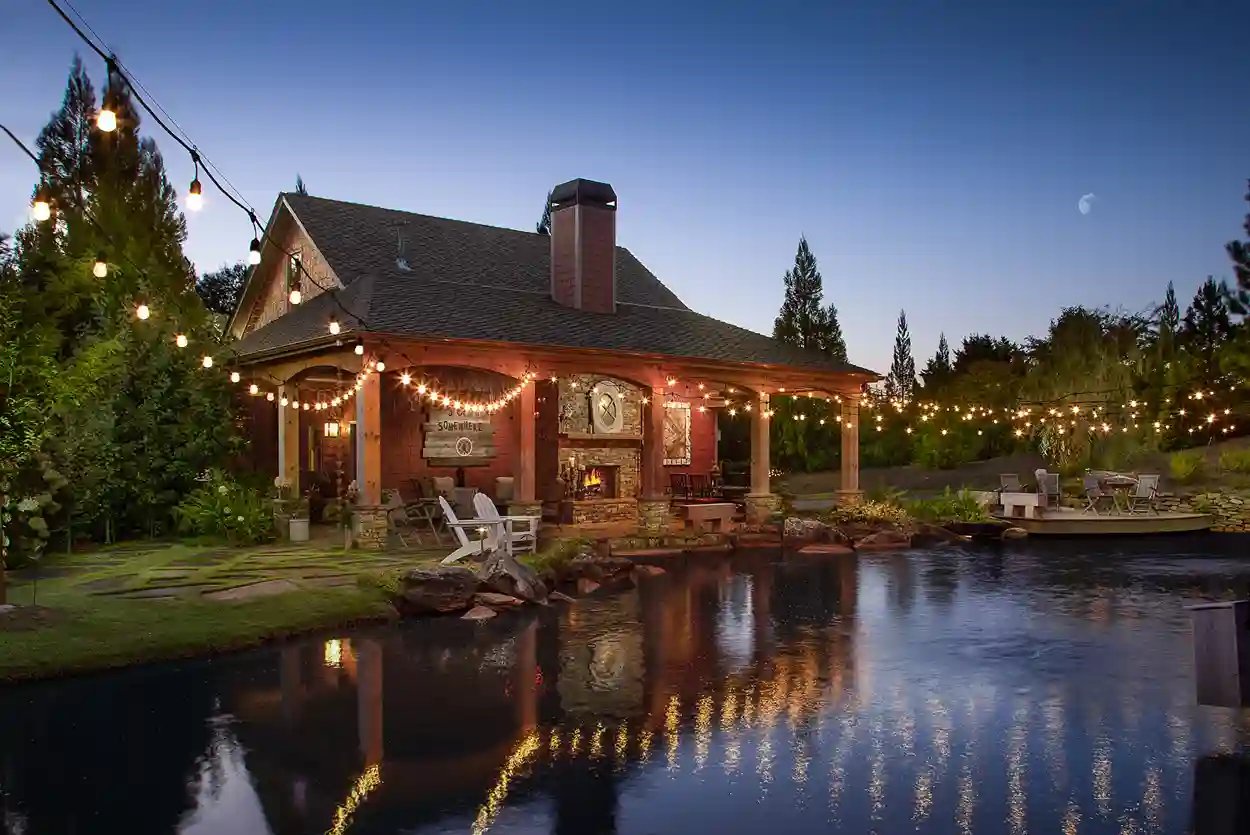 Enchanting evening at a lakeside home with illuminated string lights and a cozy outdoor fireplace.