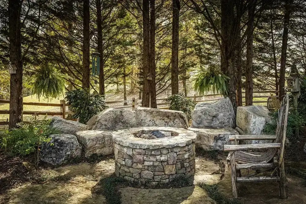 Custom outdoor stone fire pit with rustic seating in a landscaped garden by Michael James Remodeling.