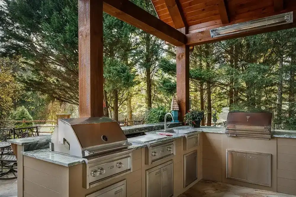 Outdoor kitchen with stainless steel grill and marble countertop under a wooden pergola