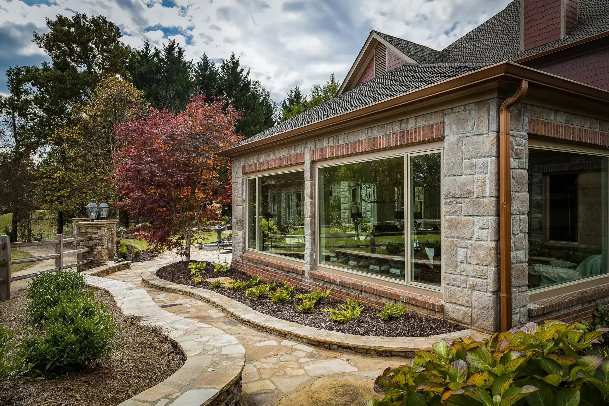 Landscaped garden path leading to a sunroom with large windows and stone accents.